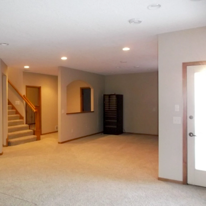 Finished basement with carpet on concrete, recessed lighting, staircase, and an arched wall niche
