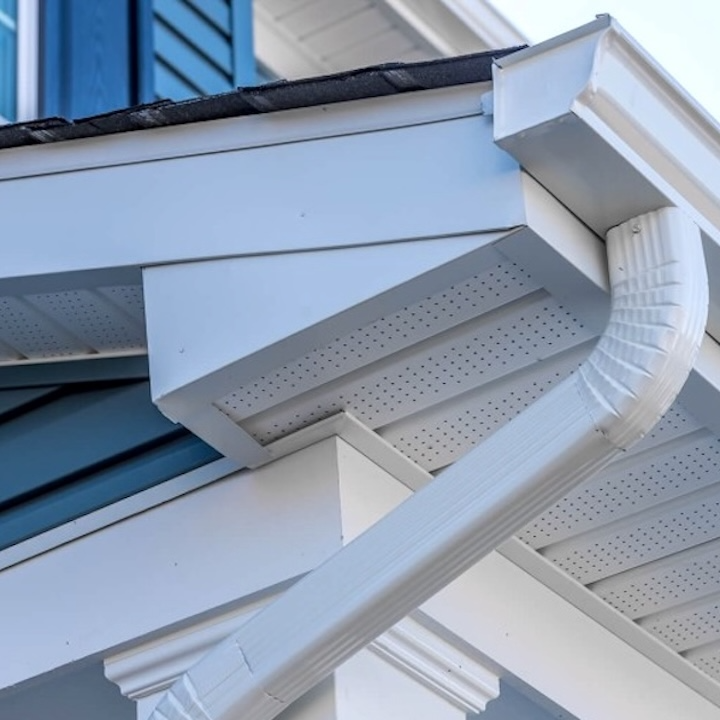 White seamless aluminum gutters and fascia wrap at a roofline corner with downspout connection